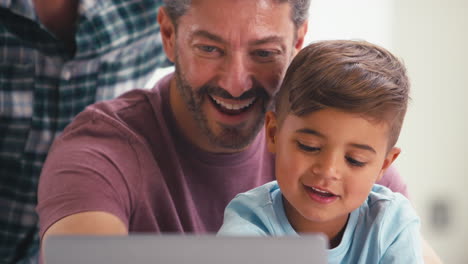 Same-Sex-Family-With-Two-Dads-And-Son-At-Home-In-Kitchen-Using-Laptop