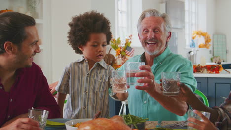 Multi-Generation-Family-Celebrating-Thanksgiving-At-Home-Eating-Meal-And-Doing-Cheers-With-Water