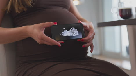 Nahaufnahme-Einer-Schwangeren-Frau-Zu-Hause-Mit-Mobiltelefon-Und-Ultraschalluntersuchung-Des-Babys