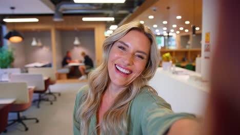 POV-Selfie-Portrait-Of-Mature-Businesswoman-In-Modern-Office-Waving-To-Mobile-Phone-Camera