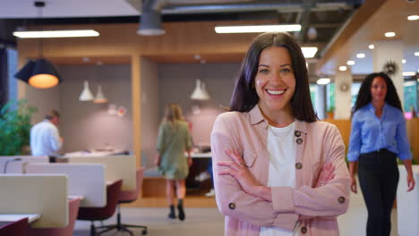 Portrait-Of-Businesswoman-Standing-In-Busy-Open-Plan-Office-With-Colleagues-In-Background