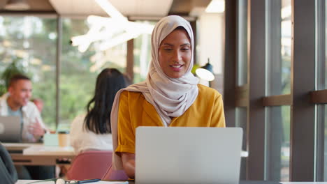 Portrait-Of-Mature-Businesswoman-Wearing-Headscarf-Working-On-Laptop-At-Desk-In-Office