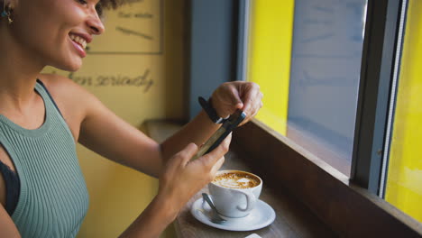 Female-Customer-In-Coffee-Shop-Window-Messaging-Using-Mobile-Phone