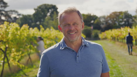 Portrait-Of-Mature-Male-Owner-Of-Vineyard-In-Field-With-Workers-At-Harvest