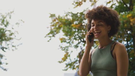 Smiling-Young-Woman-Outdoors-Laughing-As-She-Talks-On-Mobile-Phone