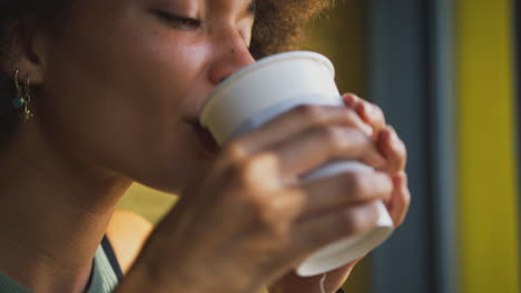 Close-Up-Of-Female-Customer-In-Coffee-Shop-Window-Drinking-Hot-Drink