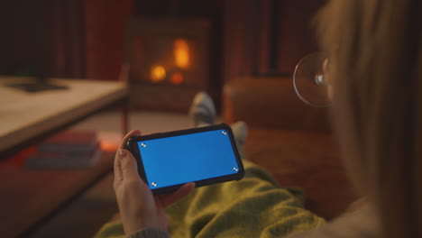 Woman-At-Home-Sitting-On-Sofa-With-Fire-Streaming-To-Blue-Screen-Mobile-Phone-Holding-Glass-Of-Wine