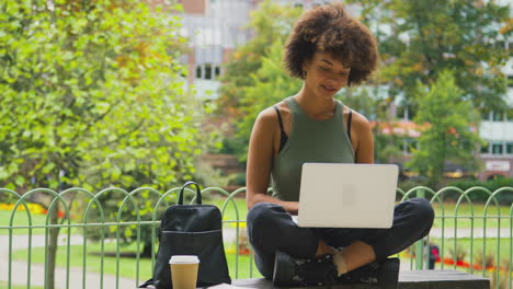 Young-Woman-Outdoors-In-Park-Sitting-On-Bench-Working-On-Laptop