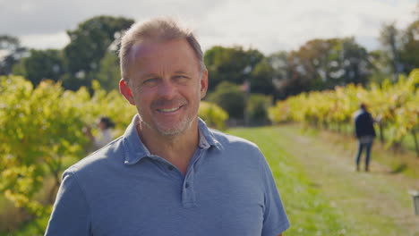 Portrait-Of-Mature-Male-Owner-Of-Vineyard-In-Field-With-Workers-At-Harvest