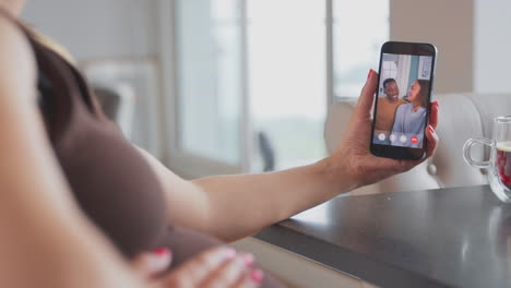Close-Up-Of-Pregnant-Woman-With-Mobile-Phone-Making-Video-Call-To-Friends-At-Home-Holding-Stomach
