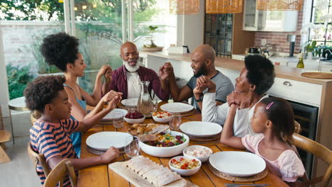 Multi-Generation-Family-Joining-Hands-And-Saying-Prayer-Before-Meal-At-Home