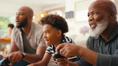Multi-Generation-Male-Family-Sitting-On-Sofa-At-Home-Playing-Video-Game-Together