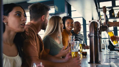 Multi-Cultural-Group-Of-Friends-In-Sports-Bar-Celebrating-As-They-Watch-Game-On-TV