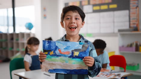 Classroom-Portrait-Of-Proud-Male-Elementary-School-Pupil-Holding-Painting-In-Art-Class-At--School