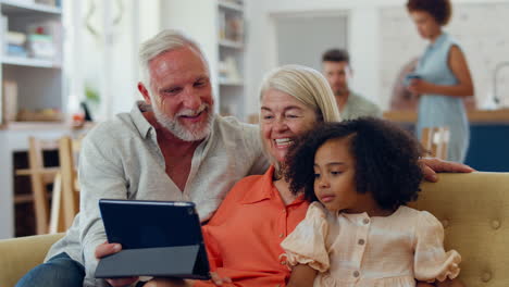 Enkelin-Und-Großeltern-Auf-Dem-Sofa-Zu-Hause,-Streaming-Show-Auf-Digitalem-Tablet