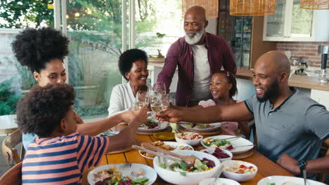 Multi-Generation-Family-Sitting-Around-Table-Doing-Cheers-With-Wine-Before-Meal-At-Home-Together