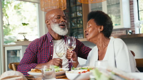Liebendes-älteres-Paar,-Das-Zu-Hause-Am-Tisch-Sitzt-Und-Gemeinsam-Eine-Mahlzeit-Mit-Wein-Genießt