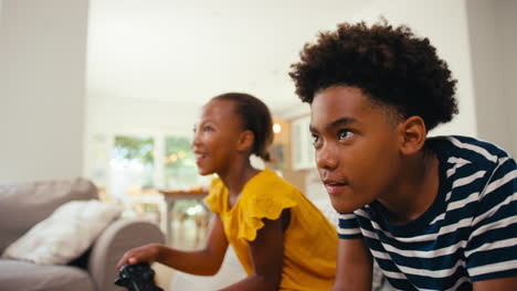 Brother-And-Sister-Sitting-On-Sofa-At-Home-Playing-Video-Game-Together-With-Girl-Winning