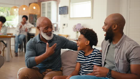 Lachende-Männliche-Mehrgenerationenfamilie,-Die-Zu-Hause-Auf-Dem-Sofa-Herumhängt-Und-Miteinander-Redet