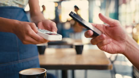 Close-Up-Of-Man-In-Coffee-Shop-Paying-Bill-With-Contactless-Mobile-Phone-Payment
