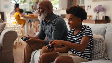Grandfather-And-Grandson-Sitting-On-Sofa-At-Home-Playing-Video-Game-Together