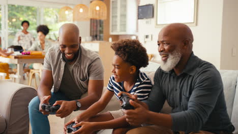 Männliche-Familie-Mit-Mehreren-Generationen-Sitzt-Zu-Hause-Auf-Dem-Sofa-Und-Spielt-Gemeinsam-Videospiele