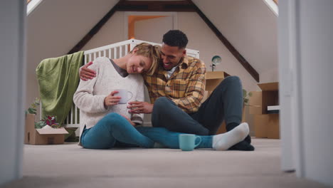 Couple-Expecting-Baby-With-Hot-Drinks-In-Nursery-Of-New-Home-Together-With-Moving-In-Boxes