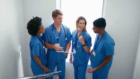 Multi-Cultural-Medical-Team-Wearing-Scrubs-Meeting-On-Stairs-In-Hospital-Discussing-Patient-Chart