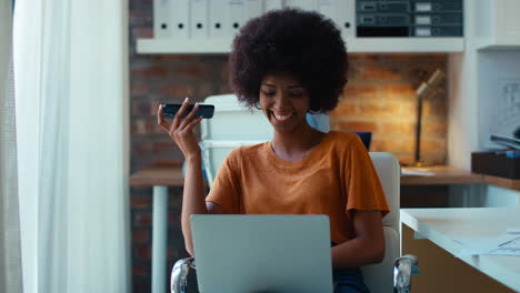 Young-Smiling-Businesswoman-Working-At-Desk-In-Office-Talking-Into-Mic-Of-Mobile-Phone