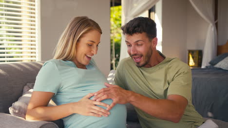 Couple-With-Pregnant-Woman-In-Bedroom-At-Home-With-Man-Feeling-Baby-Kicking