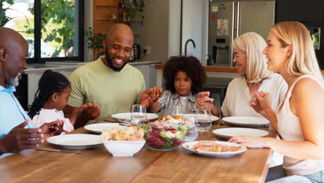 Familia-Multigeneracional-Tomándose-De-La-Mano-Y-Rezando-Antes-De-Comer-En-Casa