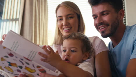 Family-Sitting-On-Sofa-At-Home-With-Parents-Reading-Book-With-Young-Son