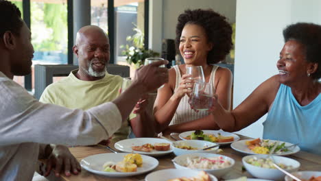 Senior-Parents-And-Adult-Offspring-Around-Table-At-Home-Doing-Cheers-With-Water-Before-Meal