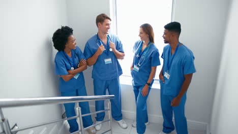 Portrait-Of-Smiling-Multi-Cultural-Medical-Team-Wearing-Scrubs-Standing-On-Stairs-In-Hospital