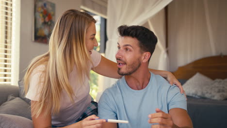 Excited-Couple-In-Bedroom-At-Home-Celebrating-Positive-Pregnancy-Test-Result