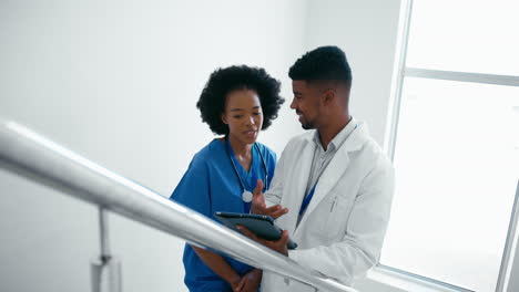 Männlicher-Arzt-Und-Krankenschwester-Mit-Digitalem-Tablet-Besprechen-Patientennotizen-Auf-Treppen-Im-Krankenhaus