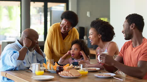 Familienaufnahme-Mit-Großeltern,-Eltern-Und-Enkelin,-Die-Beim-Frühstück-Am-Heimischen-Tisch-Grimassen-Schneiden
