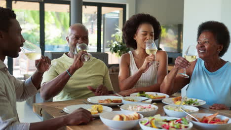 Family-Shot-With-Senior-Parents-And-Adult-Offspring-Around-Table-At-Home-Doing-Cheers-Before-Meal