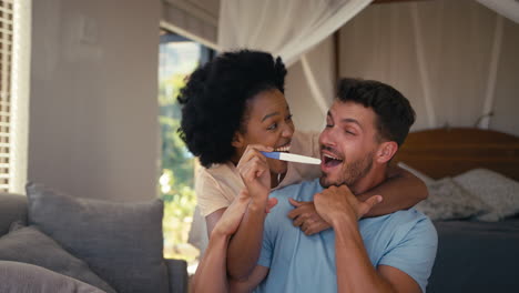 Excited-Couple-In-Bedroom-At-Home-Celebrating-Positive-Pregnancy-Test-Result