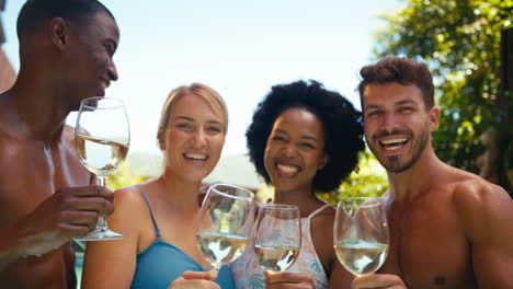 Portrait-Of-Group-Of-Smiling-Multi-Cultural-Friends-On-Holiday-In-Swimming-Pool-Drinking-Wine