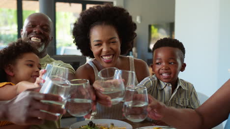 Multi-Generation-Family-Around-Table-At-Home-Doing-Cheers-With-Water-Towards-Camera
