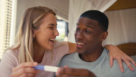 Close-Up-Of-Excited-Couple-In-Bedroom-At-Home-Celebrating-Positive-Pregnancy-Test-Result