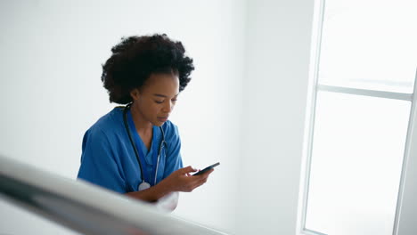Female-Doctor-Or-Nurse-Browsing-On-Mobile-Phone-On-Stairs-In-Hospital