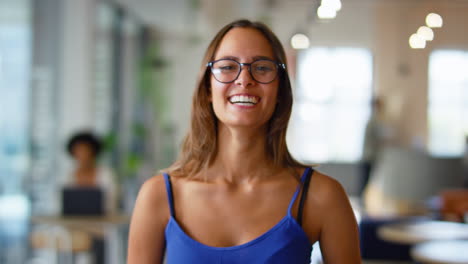 Portrait-Of-Young-Smiling-Businesswoman-Wearing-Glasses-Standing-In-Busy-Modern-Open-Plan-Office