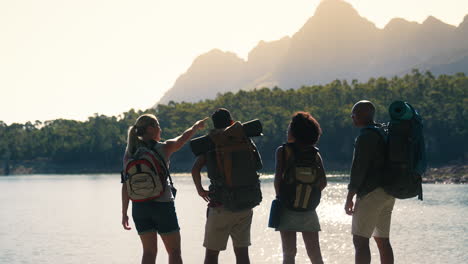 Rear-View-Group-Of-Friends-With-Backpacks-On-Vacation-Hiking-Looking-At-Lake-And-Mountains