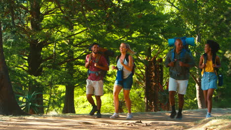 Grupo-De-Amigos-Con-Mochilas-De-Vacaciones-Corriendo-Juntos-De-Caminata-Por-El-Campo-Forestal