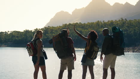 Rear-View-Group-Of-Friends-With-Backpacks-On-Vacation-Hiking-Looking-At-Lake-And-Mountains