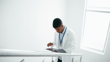 Männlicher-Arzt-Im-Weißen-Kittel-Mit-Digitalem-Tablet,-Der-Patientennotizen-Auf-Der-Treppe-Im-Krankenhaus-überprüft
