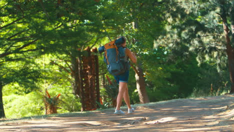 Woman-With-Backpack-Waving-As-She-Sets-Off-On-Vacation-Hiking-Through-Countryside