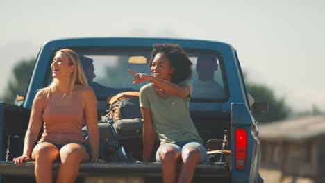 Zwei-Frauen-Fahren-Auf-Dem-Rücksitz-Eines-Pick-up-Trucks,-Während-Freunde-Auf-Einem-Roadtrip-In-Einer-Hütte-Auf-Dem-Land-Ankommen